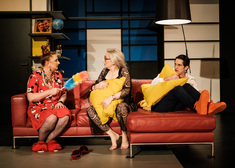 trójka aktorów siedzi na czerwonej kanapie.