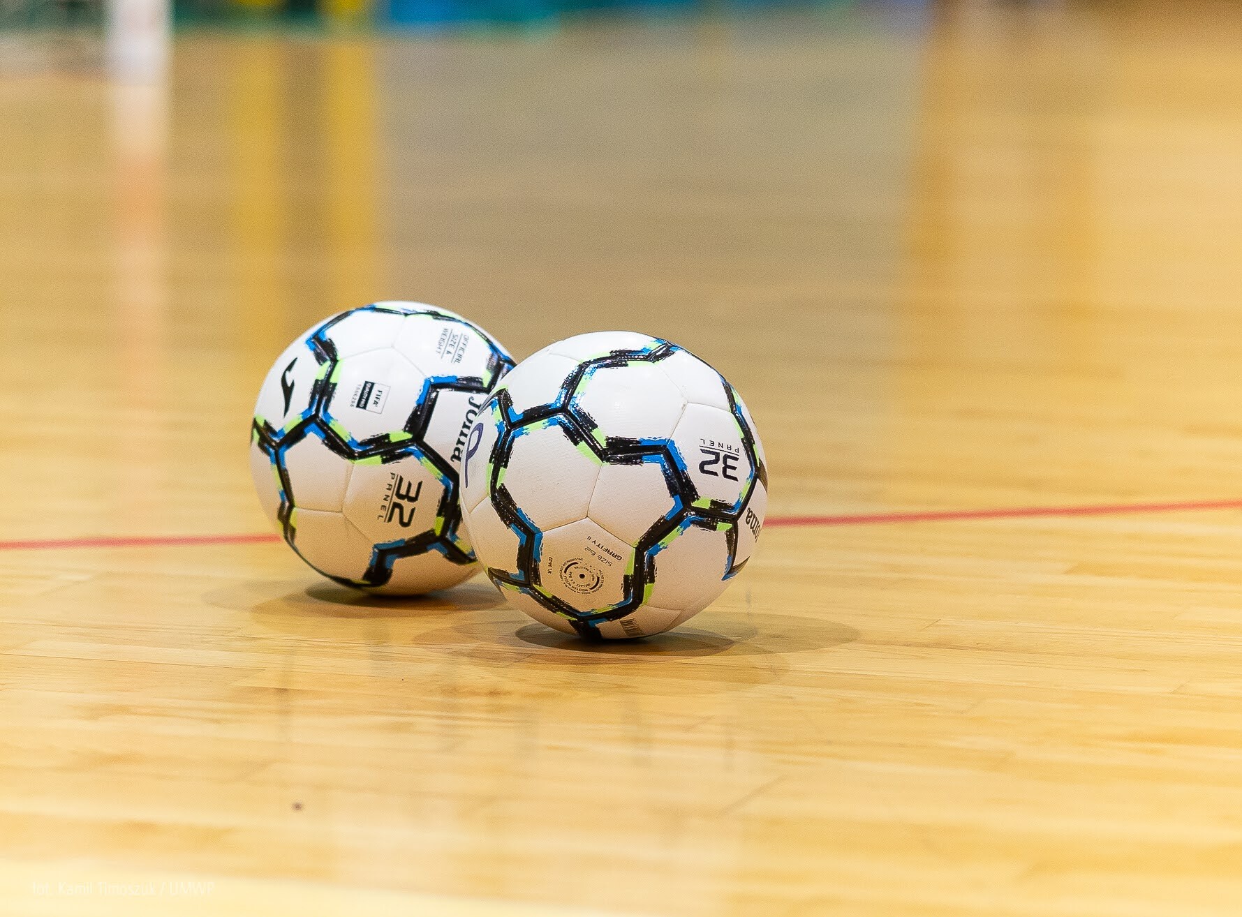 Dwie piłki leżą na podłodze hali sportowej.