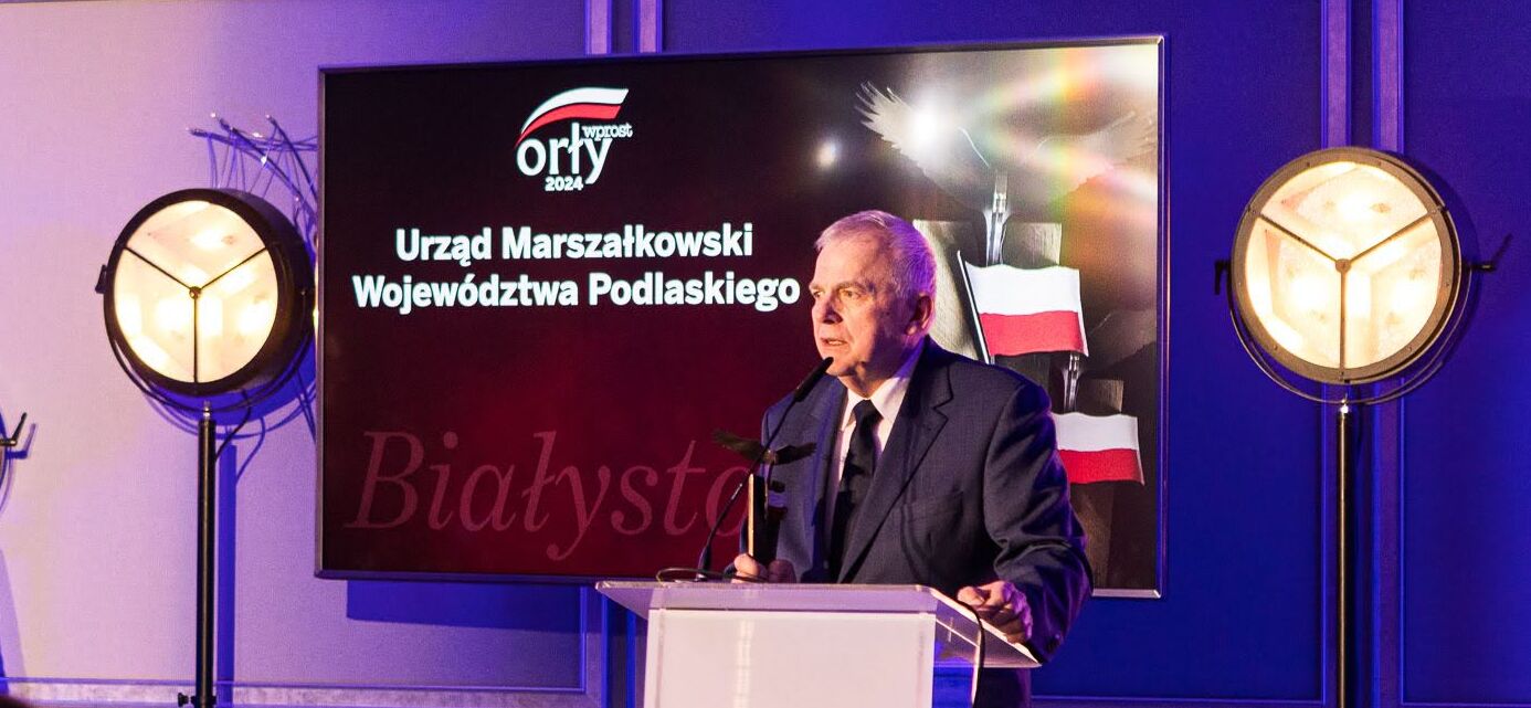 Bogusław Dębski stoi przy mównicy za nim jest telewizor wyświetlający napis urząd marszałkowski.