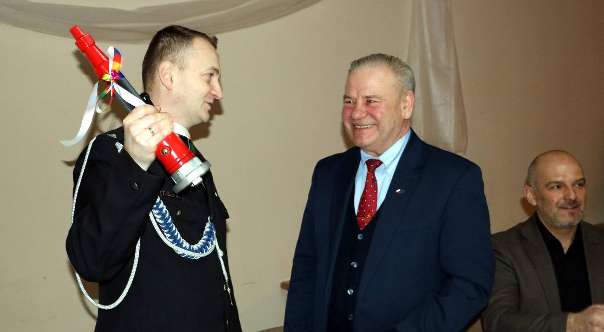 Wicemarszałek Marek Olbryś z prawej. Z lewej strażak z prądownicą w uniesionej dłoni.