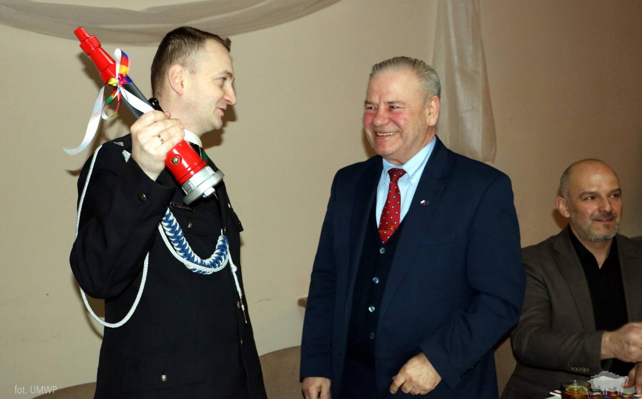 Wicemarszałek Marek Olbryś z prawej. Z lewej strażak z prądownicą w uniesionej dłoni.