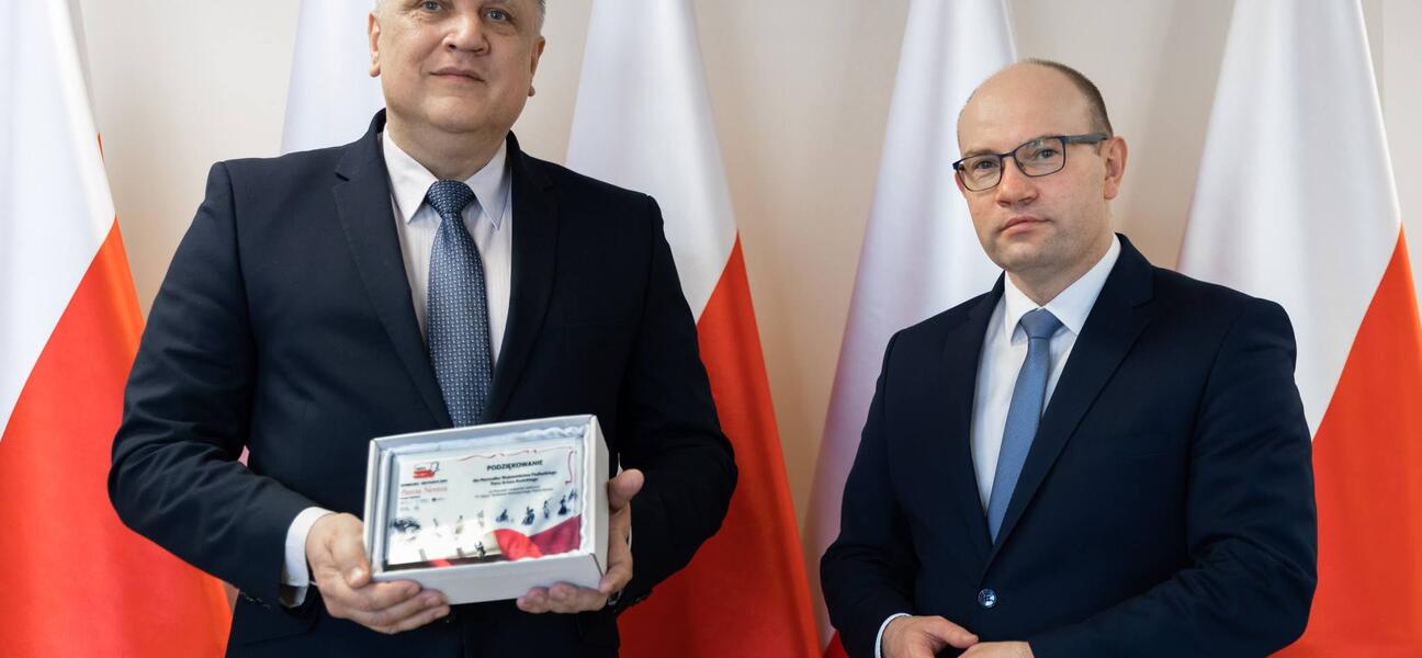 Marszałek Artur Kosicki i mężczyzna w garniturze na tle biało-czerwonych flag