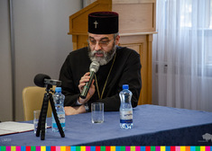 Ksiądz prawosławny przemawia siedząc przy stole.