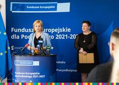 Dwie kobiety stoją na tle niebieskiej planszy Fundusze Europejskie