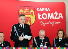 Przemawiający komendant OSP na tle herbu i napisu Gmina Łomża