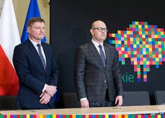 Marszałek Kosicki i członek zarządu Malinowski stoją na tle logotypu województwa podlaskiego