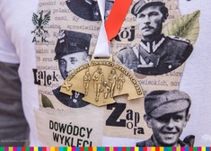 medal z X Edycji Biegu Pamięci Żołnierzy Wyklętych „Tropem Wilczym” na tle koszulki z tej samj edycji biegu