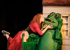 Kobieta w czerwonej sukni daje całusa żabie