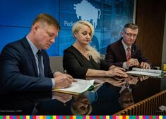 Członkowie zarządu Malinowski i Burnos siedzą przy stole konferencyjnym wraz z oficjelem