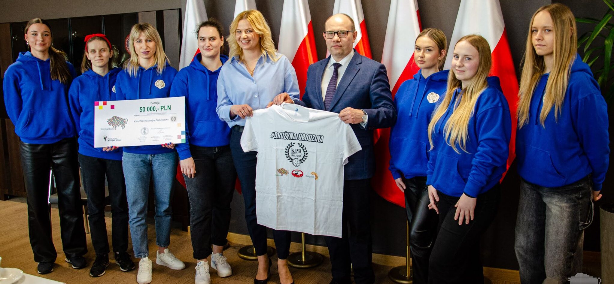 Osiem dziewczyn w niebieskich bluzach i marszałek Kosicki trzymający białą, sportową koszulkę