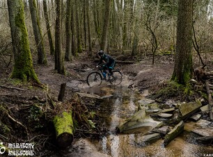 Rowerzysta przeprawiający się przez płytką, klarowną wodę w lesie