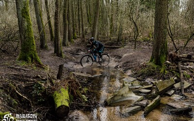 Rowerzysta przeprawiający się przez płytką, klarowną wodę w lesie