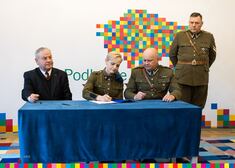 Trzy osoby w mundurach podpisują umowę, obok siedzi Marek Olbryś
