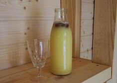 Żółty napój w butelce i pusty kieliszek na drewnianym tle