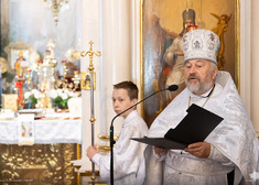 Duchowny prawosławny przy mikrofonie obok stoi chłopiec