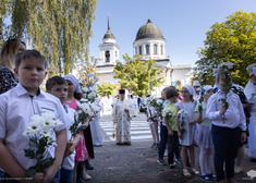 przed cerkwią grupa dzieci z kwiatami w rękach, za nimi stoi duchowny