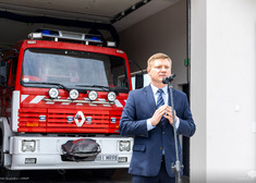 Marek Malinowski przemawia do mikrofonu na tle wozu strażackiego