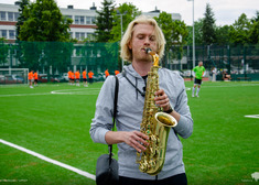 Chłopak gra na saksofonie na tle boiska.