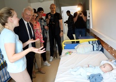 Oficjele i rodzice dziecka stoją nad szpitalnym łóżkiem.