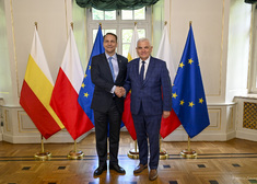 Minister Radosław Sikorski stoi na tle flag z prezydentem Tadeuszem Truskolaskim i ściska jego dłoń