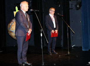 Dwóch mężczyzn stoi na scenie przed nimi mikrofony