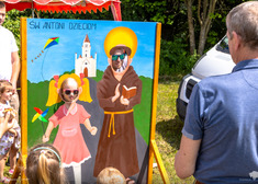 Rodzic z dzieckiem robią zdjęcia wkładając głowy do obrazu ze św. Antonim i dzieckiem