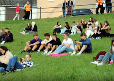 Widzowie siedzą na trawie.