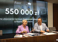 Wiesława Burnos wraz z mężczyzną siedzącym obok podpisują umowy.