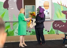 Dyrektor placówki przekazuje wiązankę kwiatów osobie w masce goblina