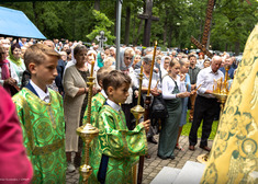 Chłopcy wystrojeni w szaty liturgiczne. Za nimi tłum wiernych