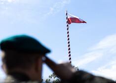Na pierwszym planie widać żołnierza salutującego przed flagą na maszcie