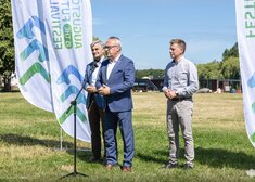 Burmistrz Augustowa zabiera głos stojąc między dwoma mężczyznami 