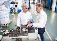 Dwaj mężczyźni rozmawiają przy jedenj z maszyn znajdujących sie na terenie hali produkcyjnej przedsiębiosrtwa, w których odbywa sie wydarzenie