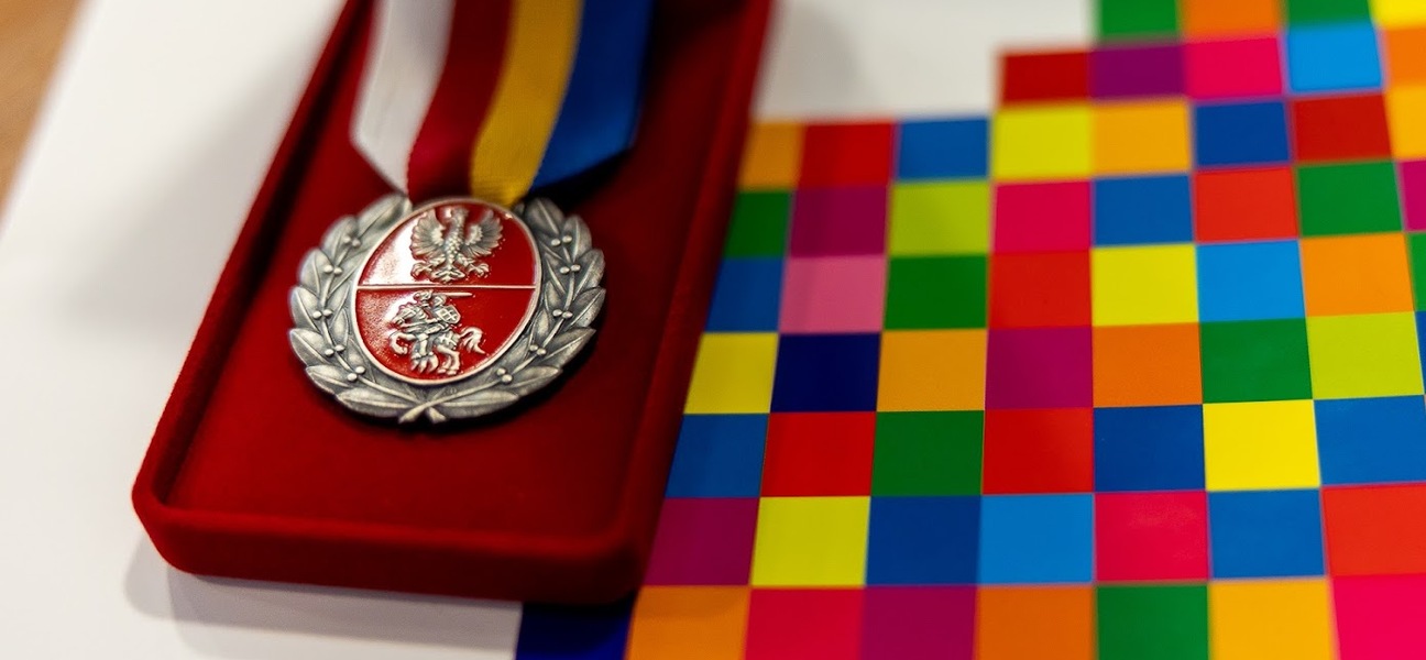 Medal na aksamitnej podstawce, obok leży teczka w kolorowe kwadraty