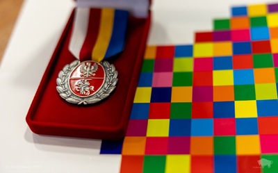 Medal na aksamitnej podstawce, obok leży teczka w kolorowe kwadraty