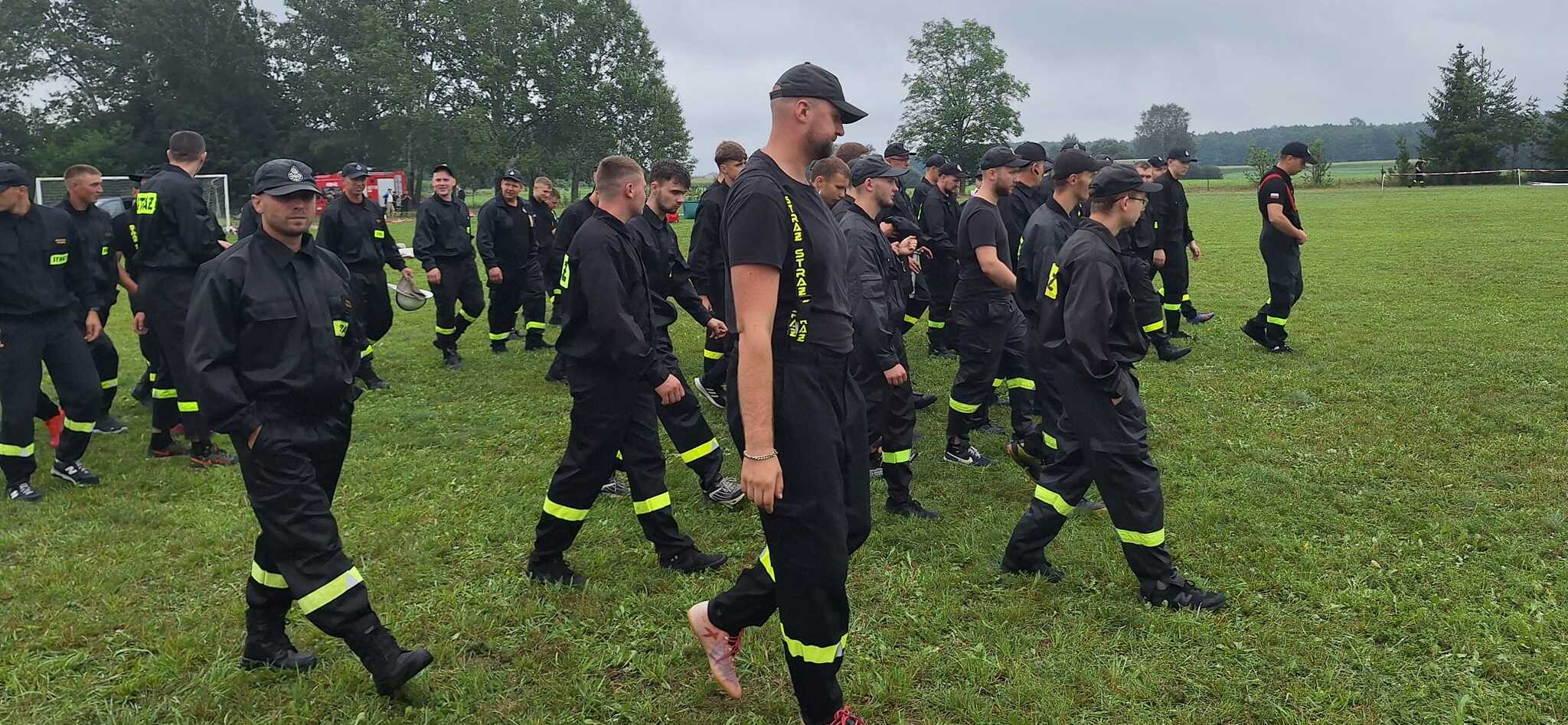 Strażacy w dużej grupie idą przez plac