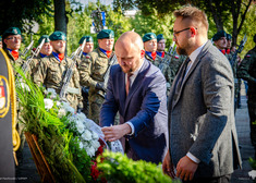 Łukasz prokorym poprawia wstążkę przy wieńcu.