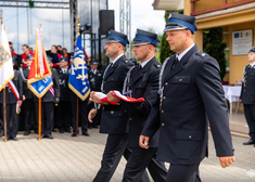 Trzech strażaków maszeruje ze złożoną biało-czerwoną chorągwią