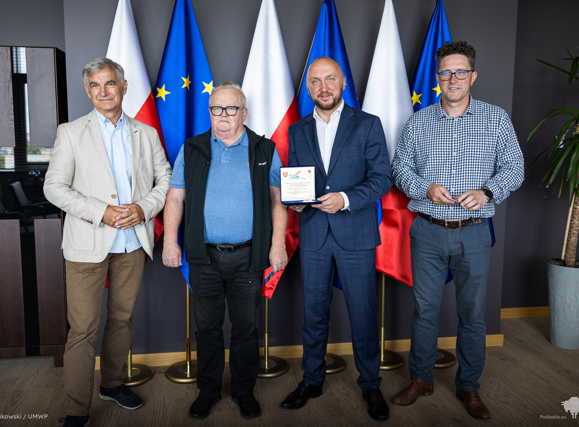 Dwóch przedstawicieli zarządu województwa oraz Wojciech Fortuna i prezes WOSiRu stoją na tle flag