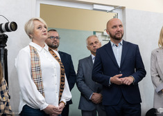 Oficjele słuchają wypowiedzi stojąc w grupce przy futrynie.