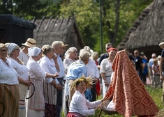 Ludzie w strojach ludowych przed domkami z epoki.