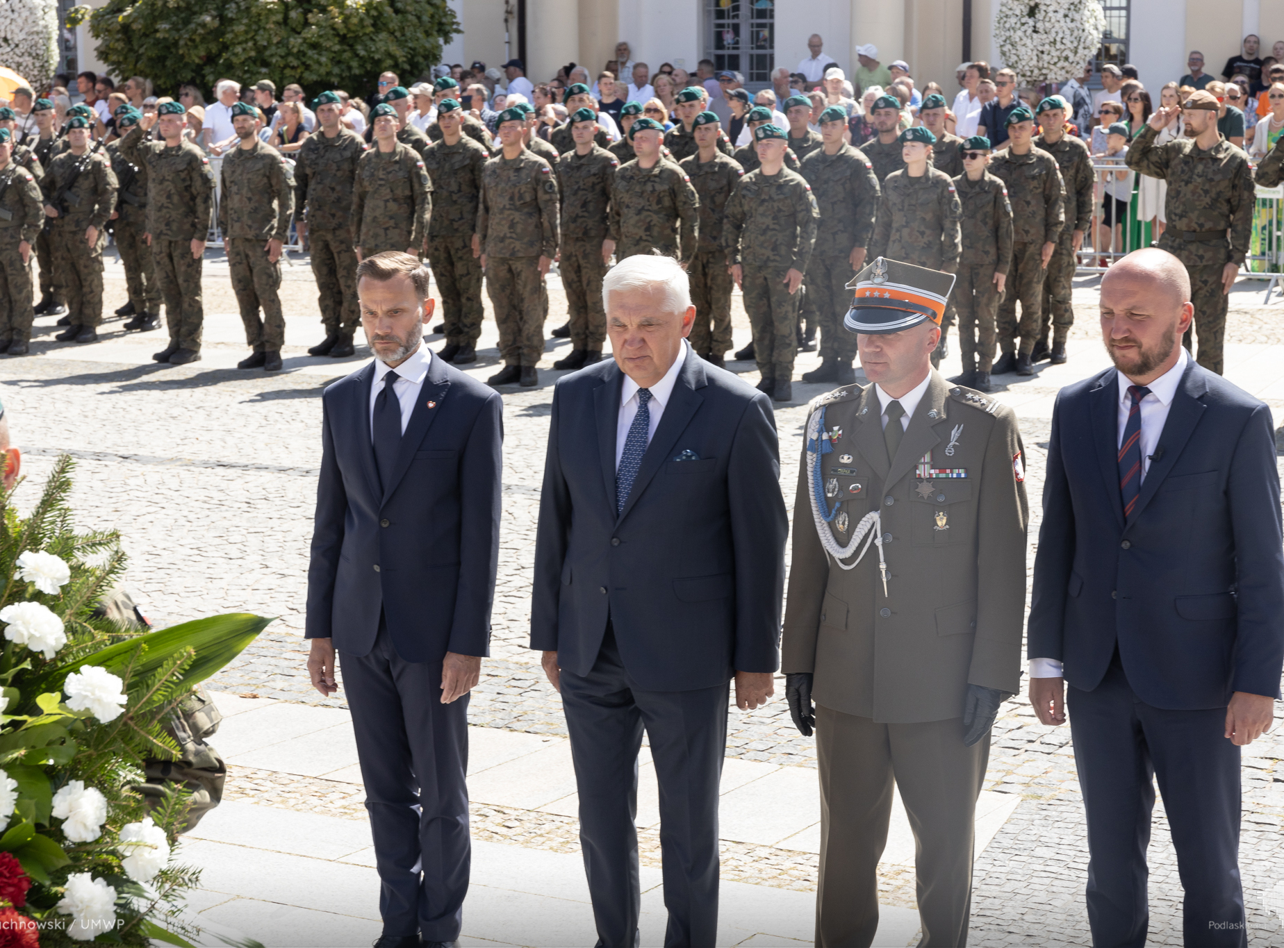 Oficjele stoją na baczność. W ich tle żołnierze stoją w formacji.