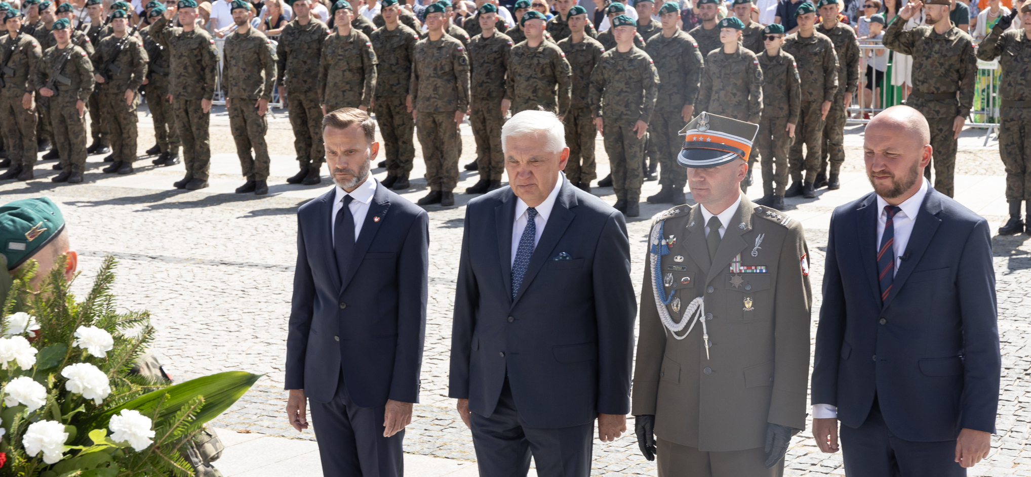 Oficjele stoją na baczność. W ich tle żołnierze stoją w formacji.