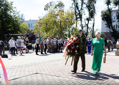 Wiesława Burnos podchodzi podchodzi do pomnika wraz z żołnierzem trzymającym wieniec.