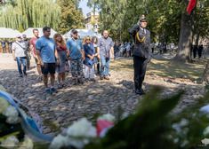 Ludzie stoją na baczność przed pomnikiem