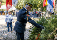 Strażnik miejski poprawia wieniec, za nim stoi kobieta.