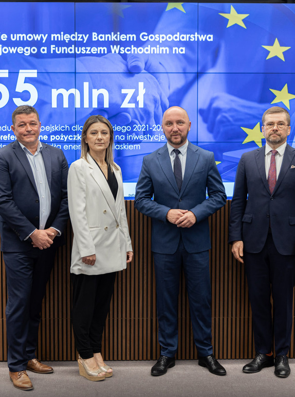 Czterech uczestników konferencji na tle planszy z kwotą na pożyczki.