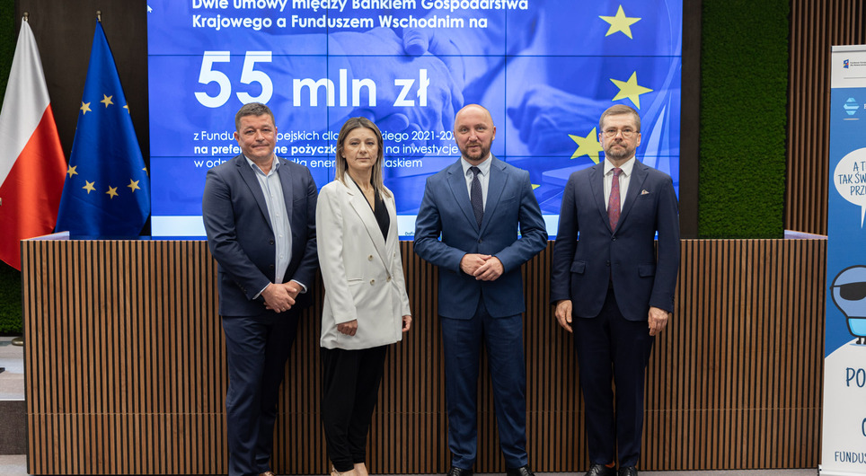 Czterech uczestników konferencji na tle planszy z kwotą na pożyczki.