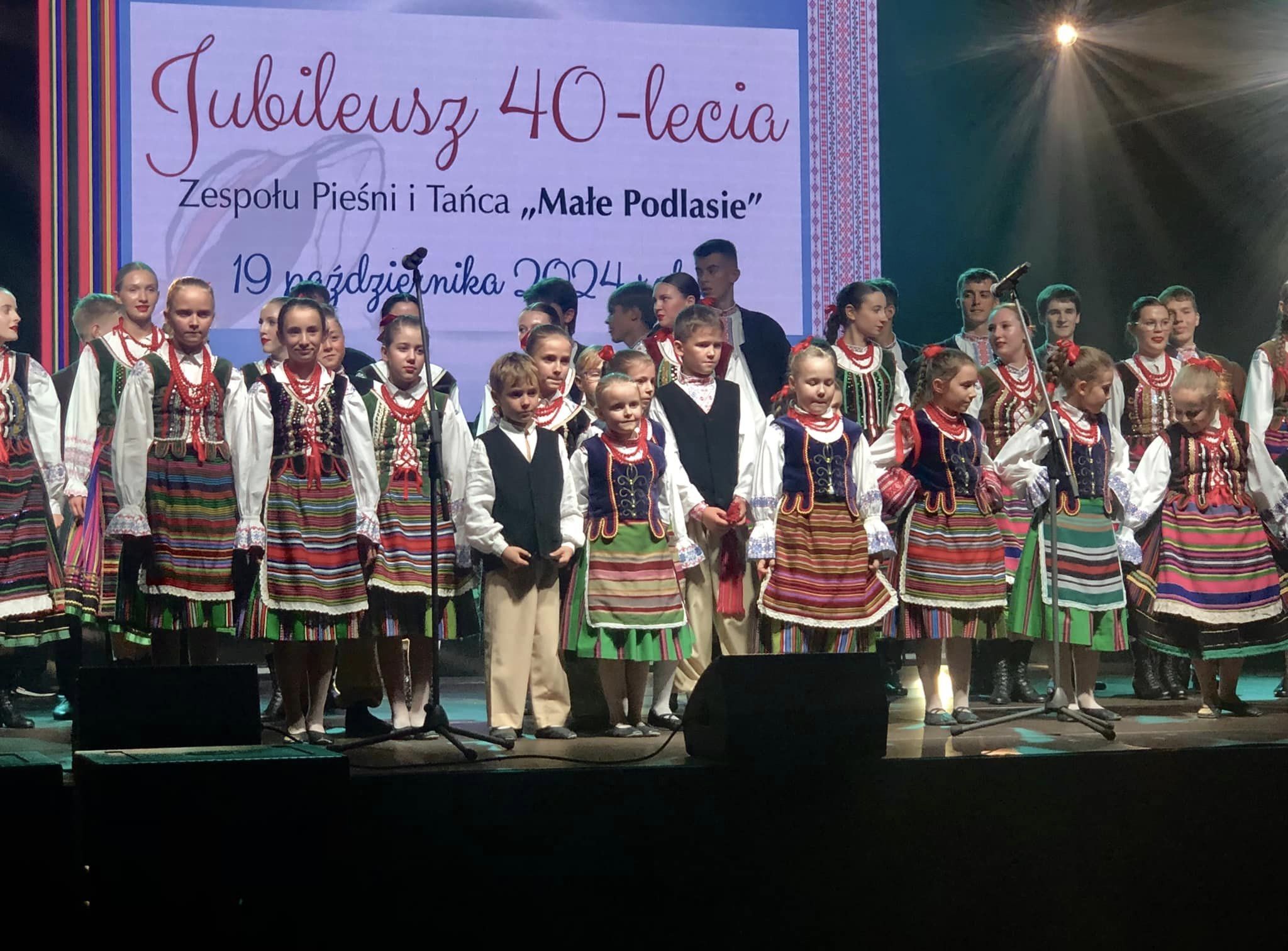 Dzieci w strojach ludowych stoją na scenie