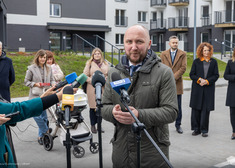 Kolejny mężczyzna przemawia, kilkanaście słucha, w tle widok bloków mieszkaniowych